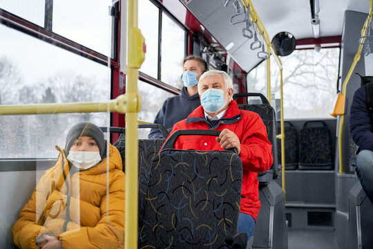 Front view of passengers sitting on bus, wearing medical masks, protecting from global pandemic. People traveling by public transport, looking forward. Concept of urban life.