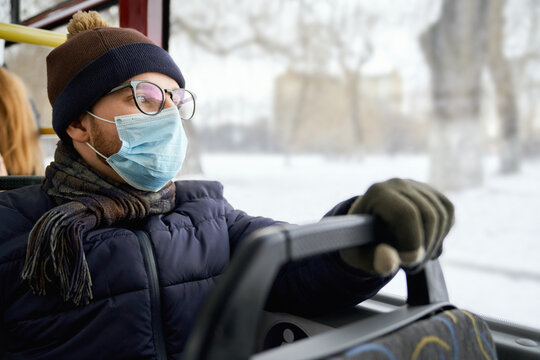 Side view of passenger traveling by bus during global pandemic, wearing medical mask, protecting. Young man wearing glasses, sitting, holding. Conept of quarantine measures.