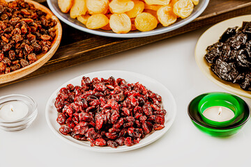 Ramadan food composition with dried apricots, cranberries, raisins, and prunes on a plates on a white background with candles. Dry fruits assortment. Healthy sweet snack - mix of organic dry fruits