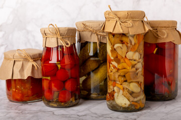 Jars of pickled vegetables cucumbers, tomatoes, mushrooms and eggplants on a light textural background. Pickled and canned foods. Copy space. Place for text.