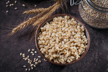 Bowl of cooked peeled barley grains porridge on dark wooden background. Cooking Healthy and diet food concept.