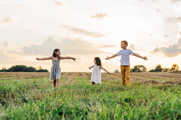 Little children stand together on field and raise arms open wide looking to each other. Carefree kids on grassy meadow.