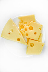 A large piece of cheese with holes on the plate. Chopped cheese and small slices on a white background. Juicy and delicious natural cheese. Cheese holes.