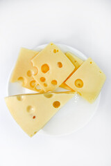 A large piece of cheese with holes on the plate. Chopped cheese and small slices on a white background. Juicy and delicious natural cheese. Cheese holes.