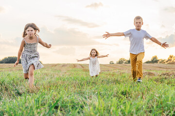 Happy little children run forward across field waving arms wide. Carefree kids on grassy meadow. Summer vacation.