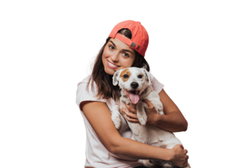 Waist up shot of caucasian young female holds tightly puppy, laughs sincerely, rejoices present from friend, likes devoted animals, wears white shirt, models over transparent background. Friendship.