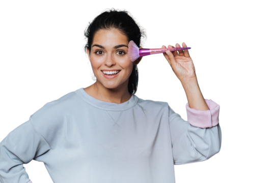 Studio shot of a casual wearing woman broad smiling and wide open eyes with a brush for makeup powder against transparent background. Beauty and cosmetics. Hispanic cheerful girl putting make up.