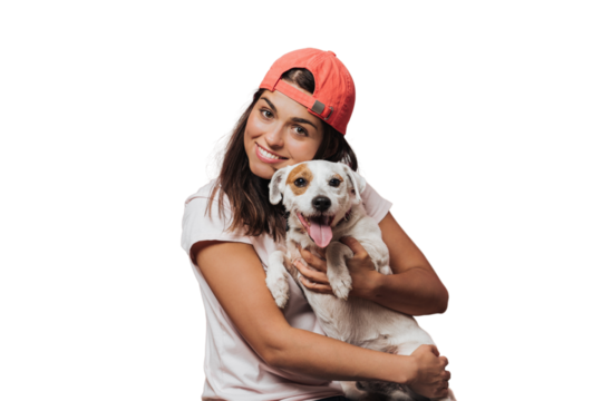 Waist up shot of caucasian young female holds tightly puppy, laughs sincerely, rejoices present from friend, likes devoted animals, wears white shirt, models over transparent background. Friendship.