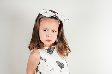 Unhappy little girl with offended facial expression. Portrait of child on white. Kid in festive...