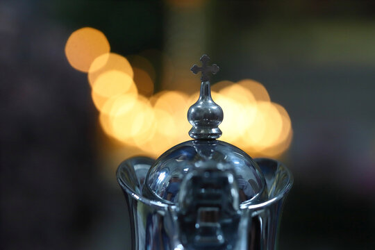 A church silver chalice with a cross against the background of the blurred light of church candles in an Orthodox church during the divine liturgy. The concept of Orthodoxy.