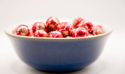 a blue bowl filled with red foil wrapped christmas chocolates balls 