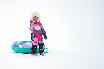 Downhill skiing. A happy child with a frosty blush on his face with an inflatable sled on a background of snow. Copy space.