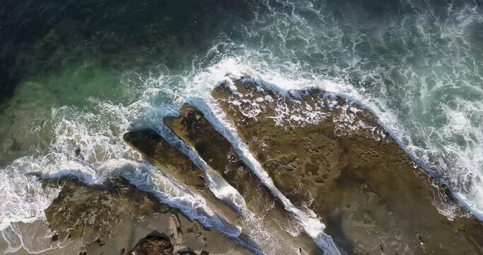 Top down aerial of waves crashing against the rocky outcrops and tide pools in La Jolla
