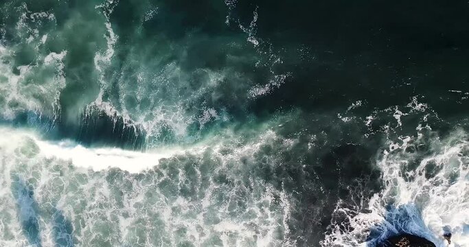 Ocean surge aerial of slow moving emerald wave crashing into rocky outcrop along the California coas