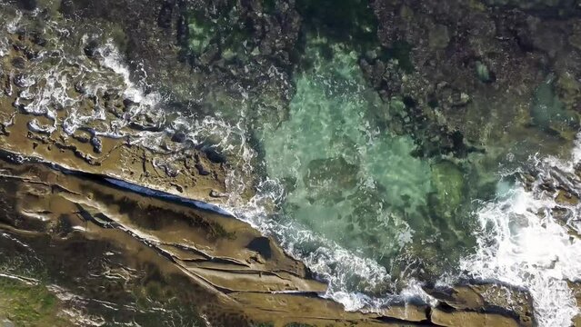Aerial footage of high tide sea waves gently enveloping colorful gem toned tide pools in La Jolla, CA 