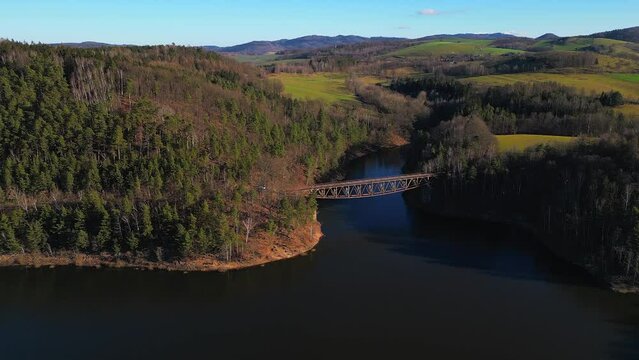 Aerial view of steel underspanned suspension railway bridge over Bobr River in Pilchowice, Wonderfull lake with islands and green forests in mountains on a sunny early spring day in Pilchowice, Poland