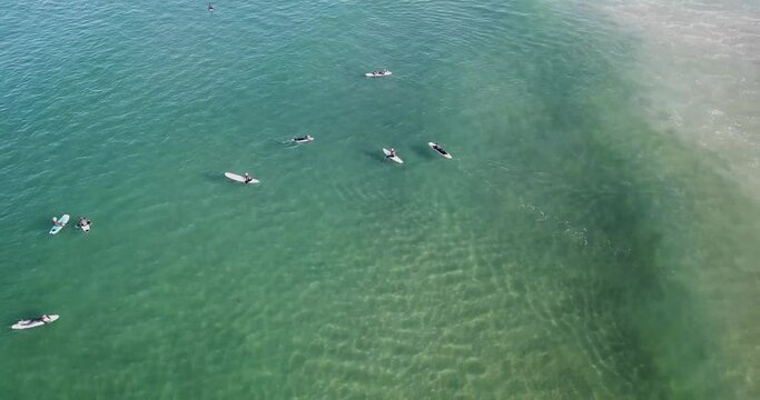 Aerial low angular perspective gliding above surfers floating on rippled Pacific waves in vibrant shades of blue and green
