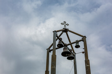 Contemporary metallic bell tower with four bells and cross in the sky