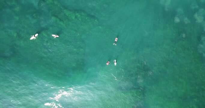 Aerial elevated zoom out over surfers and sun rays flowing through turquoise waves undulating above thriving marine life