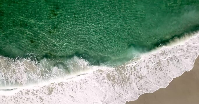 Serene emerald aqua sea spray, rippling clear and cresting waves crashing onto the sandy shore