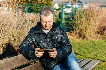 Naklejka na ściany i meble A man sits on a bench and uses a mobile phone. Wireless technologies. Communication at a distance