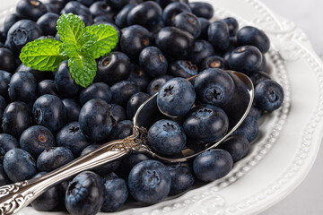 Ripe blueberry on a white plate closeup. Sweet juicy blueberries for vitamin vegan snack and vegetarian dessert. Wild berries as detox diet ingredient. Tasty summer berries.