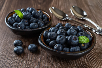 Fresh blueberry in a bowl and spoon over wooden background. Summer sweet berries for tasty fruit dessert. Sweet blueberries for vitamin healthy snack. Vegan and vegetarian concept.