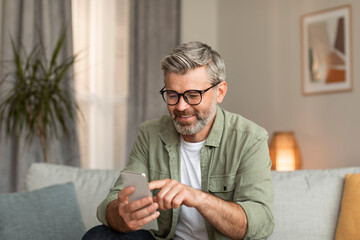 Glad elderly caucasian man in glasses typing on smartphone uses new app for communication