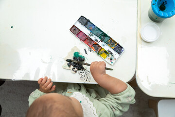 Top down view of toddler painting a blank object in montessori kindergarten