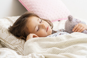 Cute little girl sleeping on bed under blanket with teddy bear. Portrait of asleep child. Morning,...