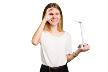 Young caucasian woman holding a small wind energy mill isolated excited keeping ok gesture on eye.