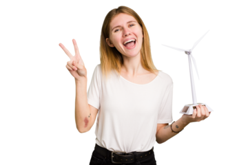 Young caucasian woman holding a small wind energy mill isolated joyful and carefree showing a peace symbol with fingers.