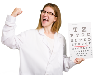 Young caucasian oculist woman holding a eye chart paper isolated raising fist after a victory, winner concept.