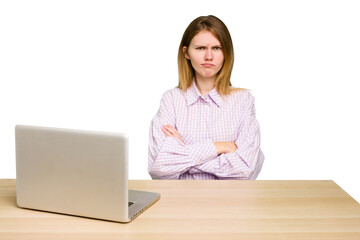 Young caucasian woman in a workplace working with a laptop isolated frowning face in displeasure, keeps arms folded.