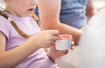 Anonymous elementary school age child girl eating ice cream from a small white blank paper cup with...