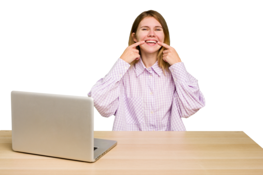 Young caucasian woman in a workplace working with a laptop isolated smiles, pointing fingers at mouth. - Powered by Adobe