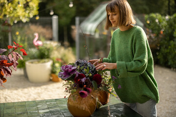 Woman arranging beautiful flowers in bouquet while standing in garden on sunny weather. Concept of floristry and garden hobby