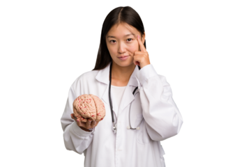 Young asian doctor woman holding a brain isolated pointing temple with finger, thinking, focused on a task.
