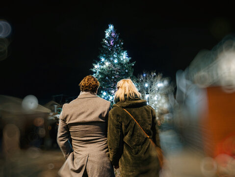 rear view of unrecognizable real couple admiring the christmas market with tall illuminated fir tree in central square of the city in Strasbourg, Alsace, France,