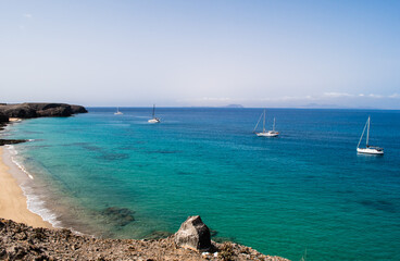 Stunning view of exotic colors on Lanzarote, Canary Islands, Spain, Europe. Turquoise color of the sea and crystalline sea. Sailboat on the horizon.
