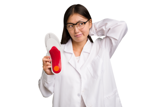 Young asian chiropodist holding a insoles for shoes isolated touching back of head, thinking and making a choice.
