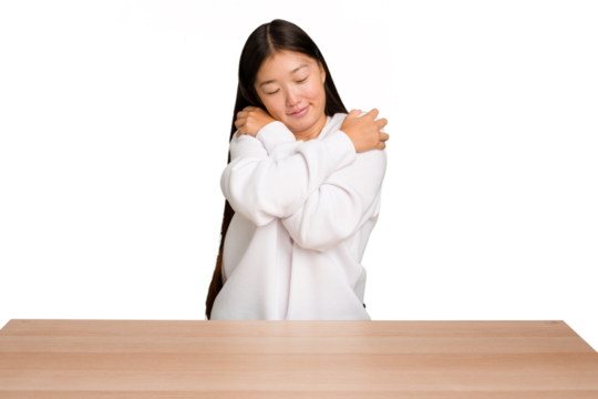 Young asian woman sitting on a table isolated hugs, smiling carefree and happy.