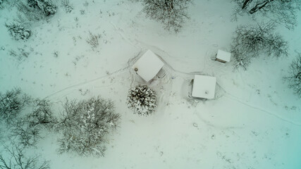 Aerial drone shot of the rooftops of a log cabin, outdoor kitchen and an outhouse covered with snow in the winter