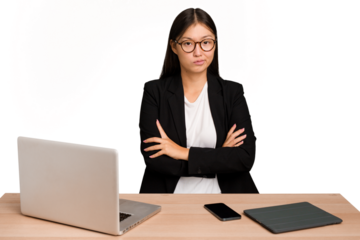 Young business asian woman sitting on a table isolated suspicious, uncertain, examining you.
