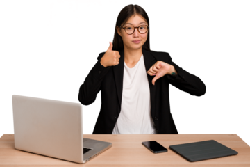 Young business asian woman sitting on a table isolated showing thumbs up and thumbs down, difficult choose concept