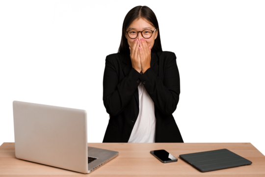 Young business asian woman sitting on a table isolated laughing about something, covering mouth with hands.