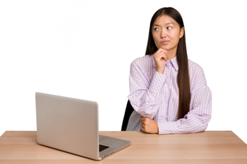 Young student asian woman in a workplace with a laptop isolated looking sideways with doubtful and skeptical expression.
