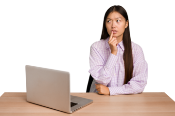 Young student asian woman in a workplace with a laptop isolated looking sideways with doubtful and skeptical expression.