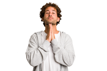 Young curly smart caucasian man cut out isolated holding hands in pray near mouth, feels confident.