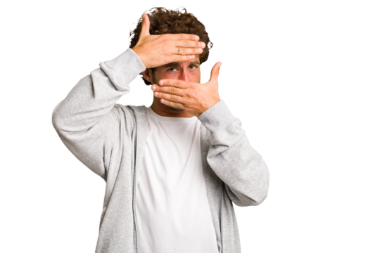 Young curly smart caucasian man cut out isolated blink at the camera through fingers, embarrassed covering face.